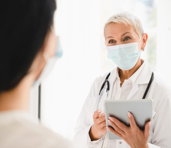Senior female doctor gynecologist in protective face mask against coronavirus Covid 19 talking with patient about diagnosis recovery test results in hospital