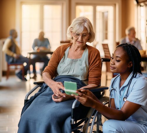 Senior woman in wheelchair her pills with help of African American nurse at residential care home.